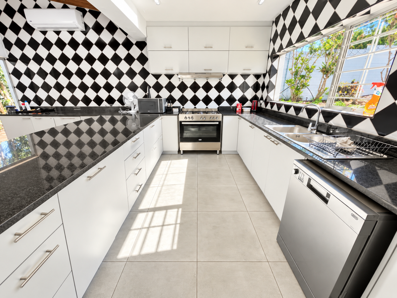 Modern kitchen featuring white cabinetry, black granite countertops, a stainless steel gas stove, and a striking black and white checkered tile backsplash.