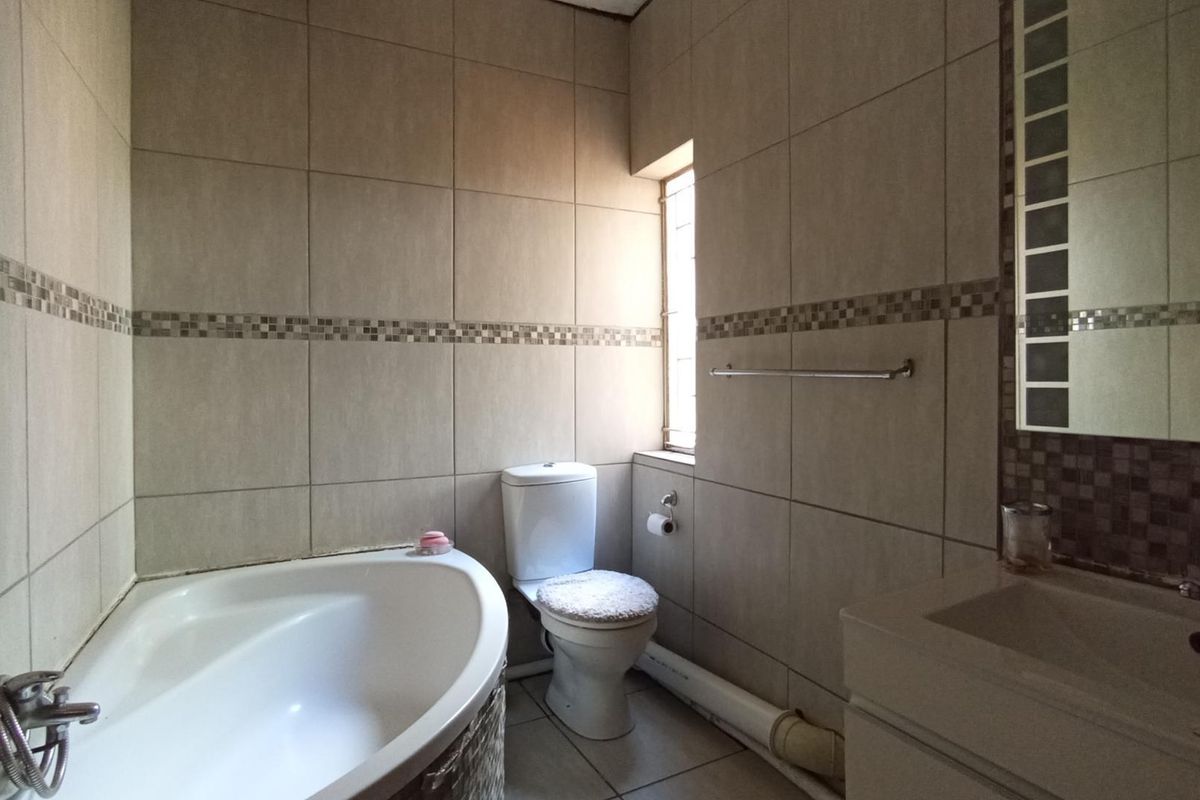 A functional bathroom featuring a built-in bathtub, toilet, and vanity basin with tiled finishes and a wall-mounted mirror.