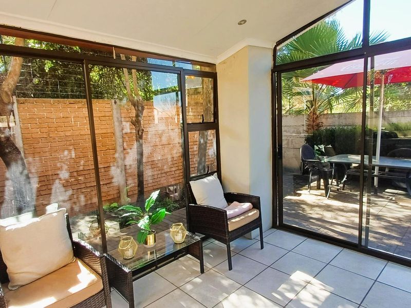 A bright, enclosed patio area featuring large sliding glass doors, tiled flooring, and direct access to the rear garden space.