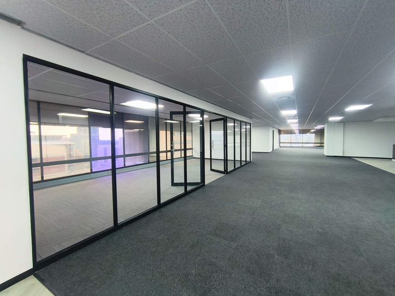 Spacious open-plan office area featuring modern glass partitions, suspended ceilings with recessed lighting, and clean carpeted flooring throughout.