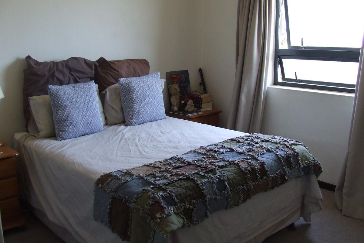 A bedroom featuring neutral walls, carpeted flooring, and a top-hung window with integrated curtain tracks.