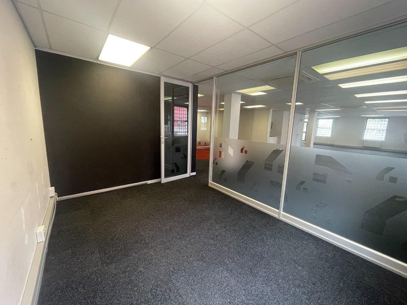 A vacant office space featuring a modern glass partition, dark accent wall, carpeted flooring, and recessed lighting in a suspended ceiling.