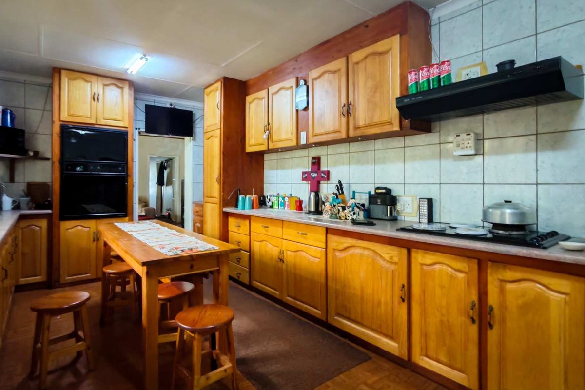 A functional kitchen featuring extensive wooden cabinetry, built-in oven, integrated hob, and a tiled backsplash, offering ample storage and workspace.