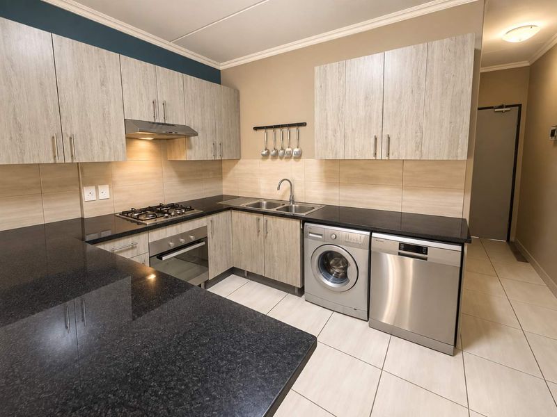 Modern kitchen featuring light wood-grain cabinetry, dark granite countertops, integrated gas hob, oven, and dedicated spaces for laundry and dishwasher appliances.