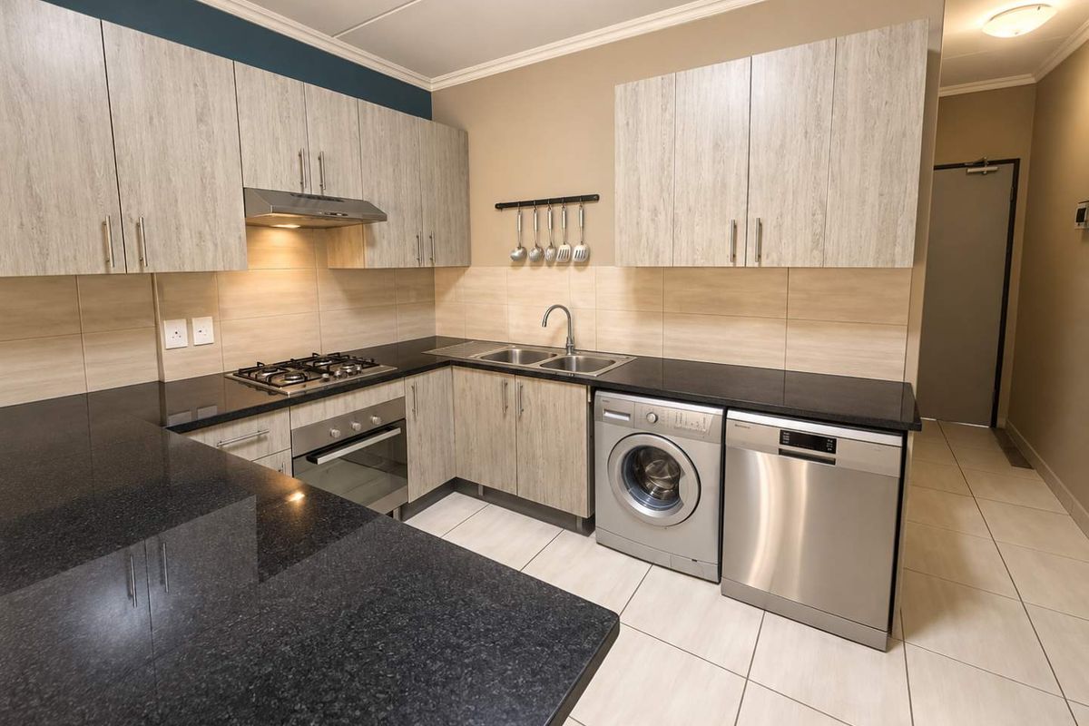 Modern kitchen featuring light wood-grain cabinetry, dark granite countertops, integrated gas hob, oven, and dedicated spaces for laundry and dishwasher appliances.