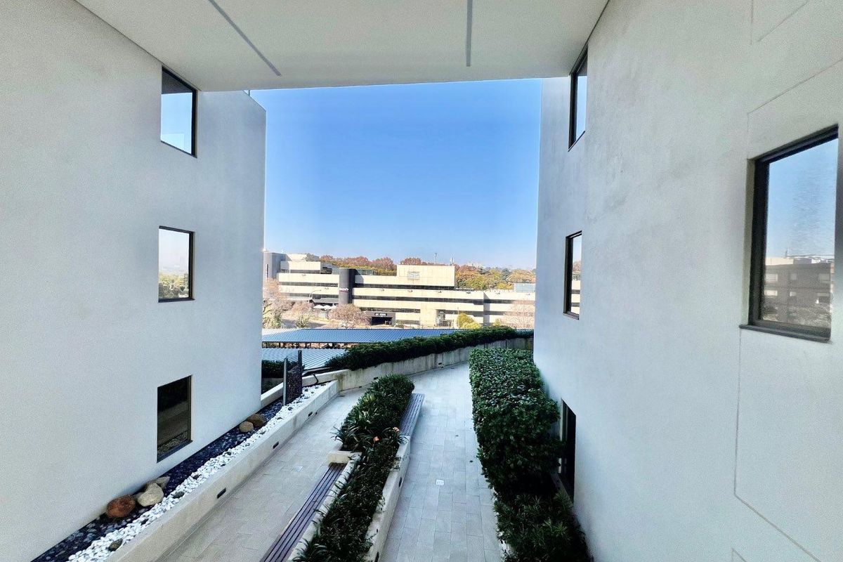 A modern, well-maintained outdoor walkway between apartment building wings, featuring paved paths, integrated planter boxes, and clean architectural lines.