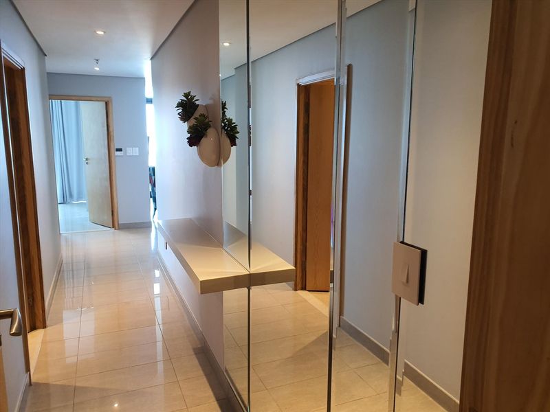 A bright, modern hallway featuring polished tiled flooring, recessed downlighting, and a sleek built-in mirror feature with a floating shelf.
