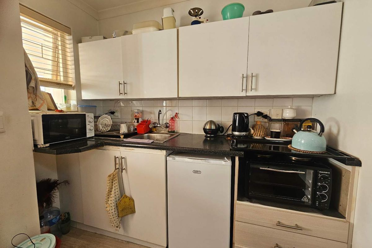 Compact kitchen featuring white laminate cabinetry, dark countertops, tiled splashback, and a built-in oven, offering a functional layout for an apartment.
