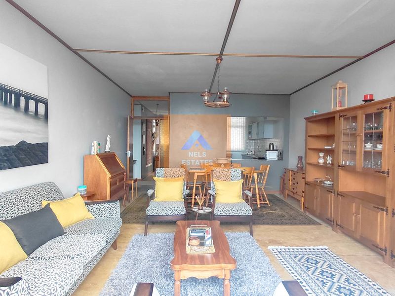 Spacious open-plan living and dining area featuring tiled flooring, exposed ceiling beams, and a connected kitchen space.