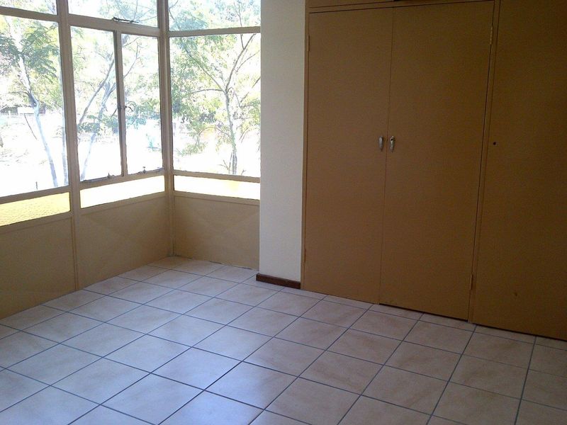 An empty bedroom featuring tiled flooring, large windows providing natural light, and built-in cupboards for storage.