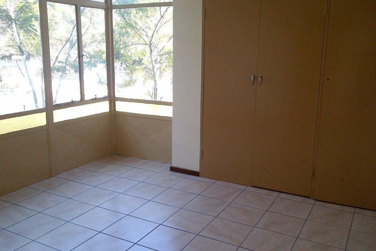 An empty bedroom featuring tiled flooring, large windows providing natural light, and built-in cupboards for storage.
