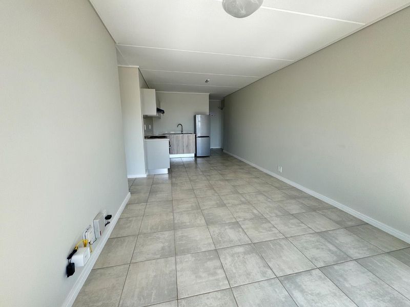 An open-plan living and kitchen area featuring neutral tiled flooring, minimalist cabinetry, and a functional layout ready for personalization.