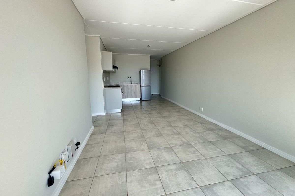 An open-plan living and kitchen area featuring neutral tiled flooring, minimalist cabinetry, and a functional layout ready for personalization.