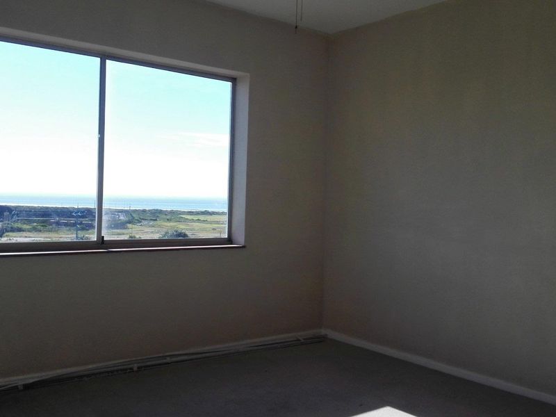 An empty bedroom featuring a large sliding window with coastal views and neutral wall finishes, ready for renovation or staging.