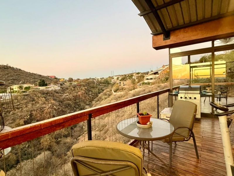 A spacious covered balcony featuring wooden decking and metal railings, offering expansive elevated views of the surrounding landscape.