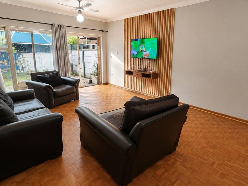 Spacious living room featuring warm parquet flooring, a modern timber slat feature wall with a floating shelf, and sliding glass doors leading to the garden.