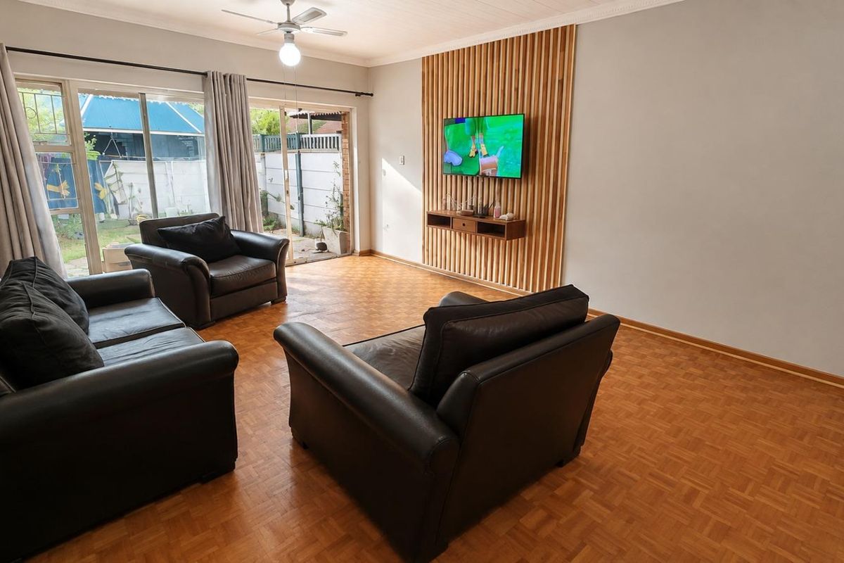 Spacious living room featuring warm parquet flooring, a modern timber slat feature wall with a floating shelf, and sliding glass doors leading to the garden.