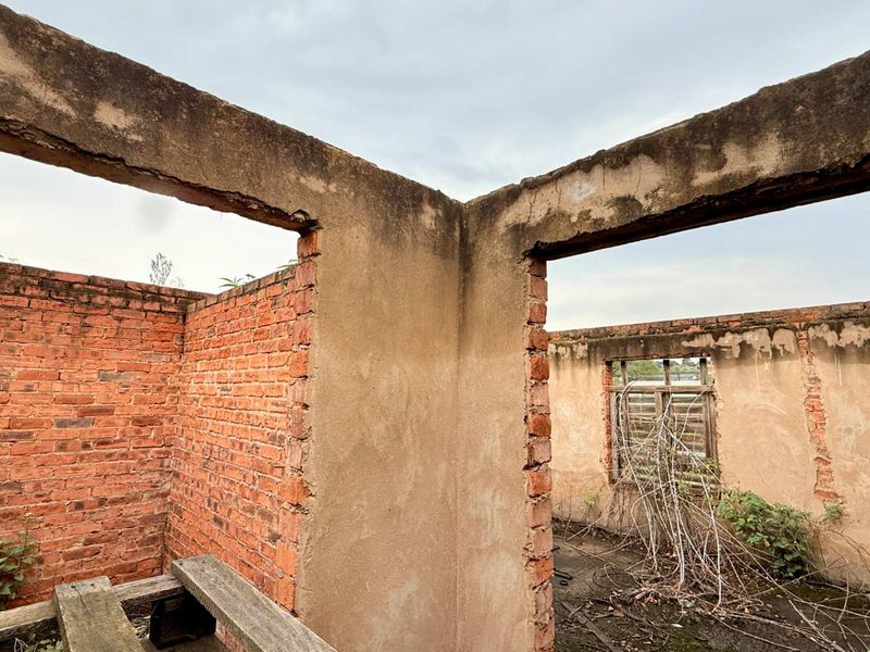 A view of a derelict structure featuring exposed brick walls and concrete lintels, showing significant signs of weathering and structural deterioration.