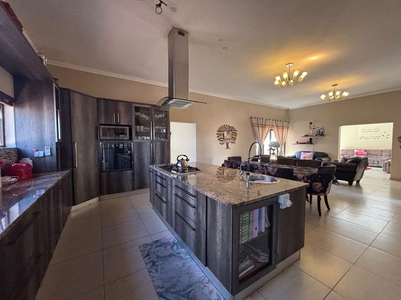 Spacious open-plan kitchen featuring a large central island with granite countertops, built-in appliances, and tiled flooring, flowing into the adjacent living and dining area.