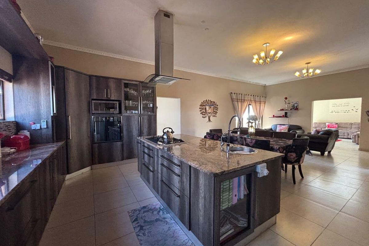 Spacious open-plan kitchen featuring a large central island with granite countertops, built-in appliances, and tiled flooring, flowing into the adjacent living and dining area.