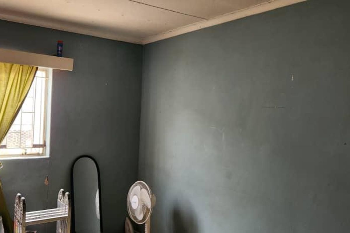 A bedroom featuring blue painted walls, a window with security bars, and ceiling cornicing, requiring cosmetic updates to improve its overall condition.