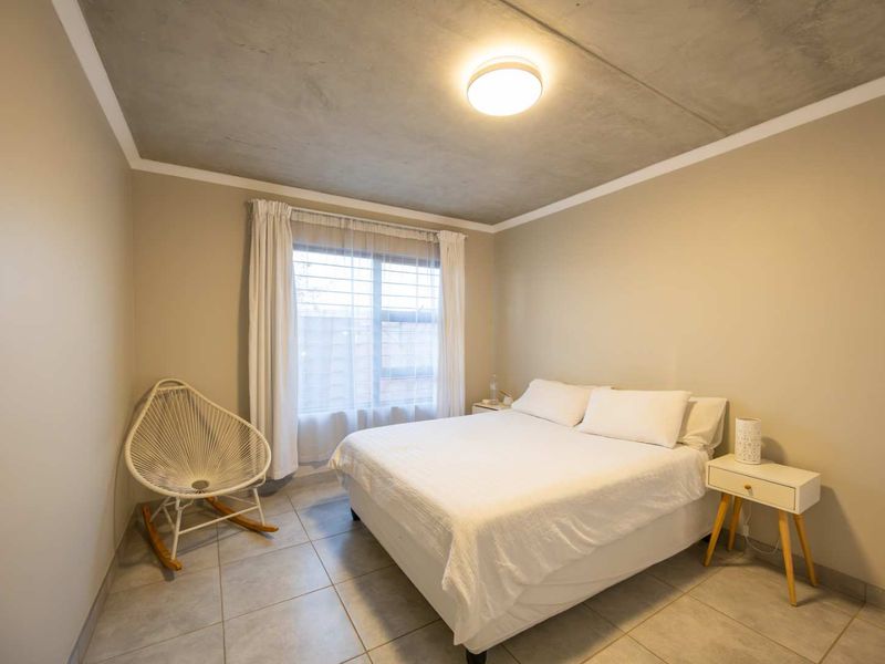 A well-lit bedroom featuring modern tiled flooring and an exposed concrete ceiling, providing a clean and contemporary aesthetic.