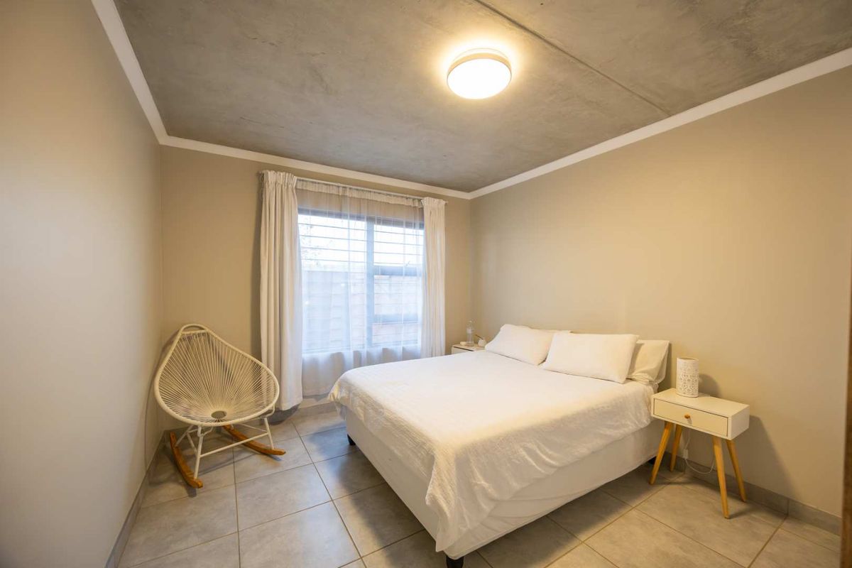 A well-lit bedroom featuring modern tiled flooring and an exposed concrete ceiling, providing a clean and contemporary aesthetic.