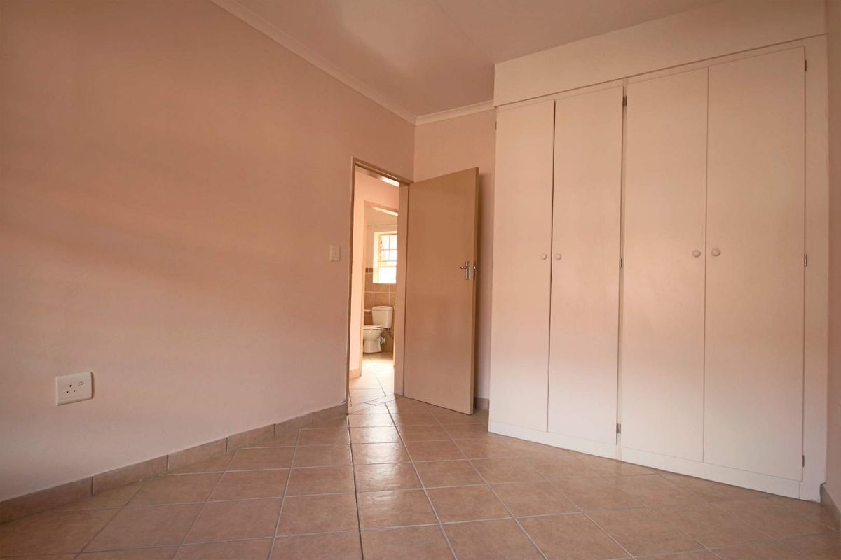 A vacant bedroom featuring neutral tiled flooring and built-in cupboards, with an adjoining view into a bathroom.