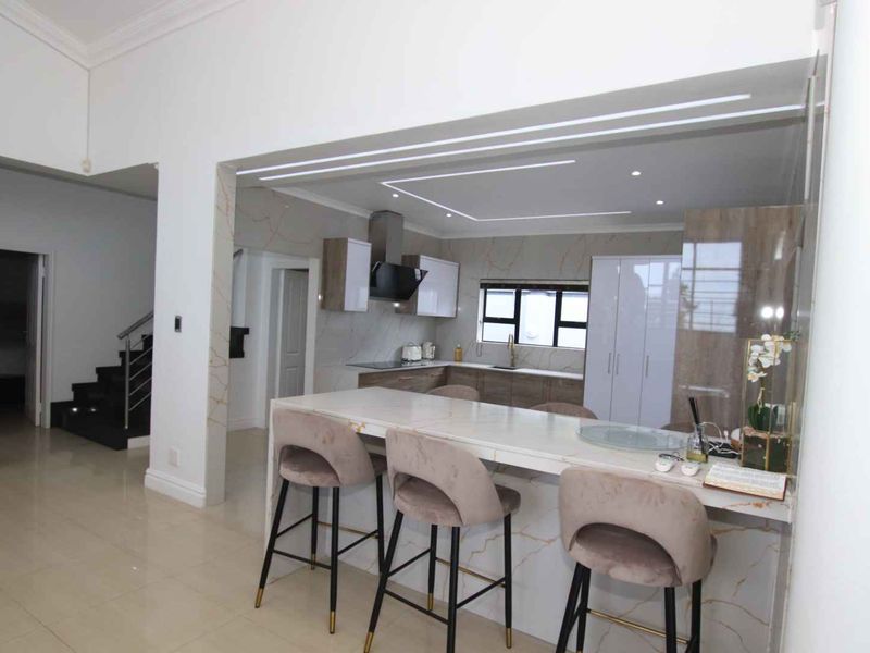 Modern open-plan kitchen featuring a stone-topped island, sleek cabinetry, and integrated lighting, seamlessly connected to the main living area and staircase.