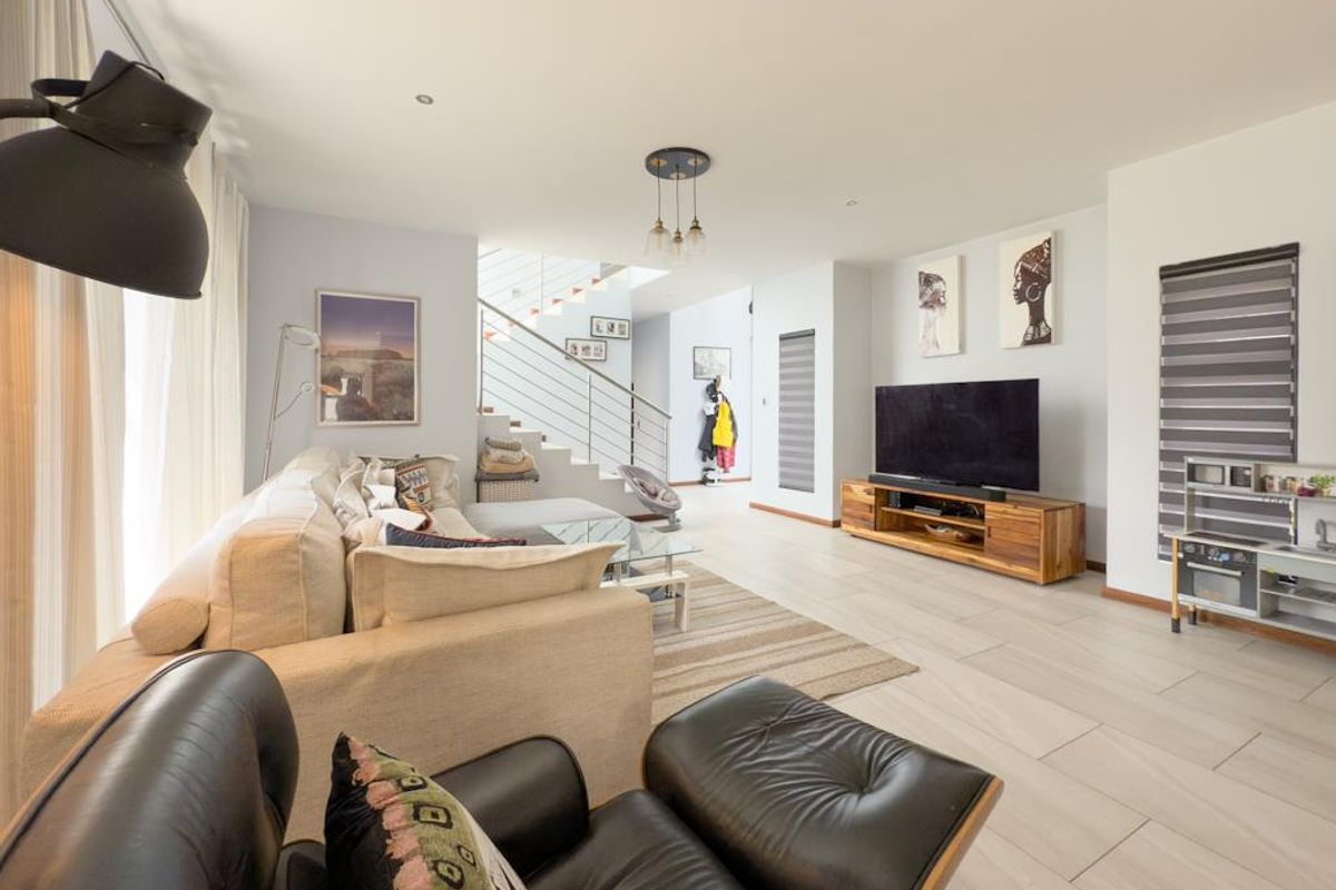 Spacious open-plan living area featuring modern tiled flooring, recessed lighting, and a staircase with a sleek metal balustrade.