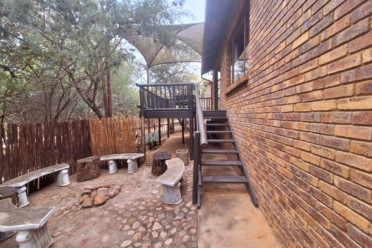 Outdoor entertainment area featuring a stone-paved patio, raised timber deck with shade sail, and a brick exterior wall.