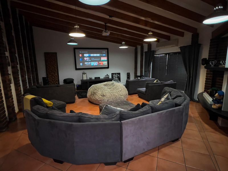 A dedicated cinema room featuring exposed timber ceiling beams, terracotta floor tiling, and a large projector screen setup.