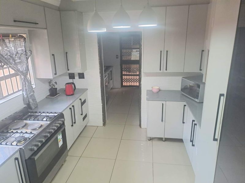 A functional kitchen featuring modern white cabinetry, grey countertops, a gas stove with oven, and tiled flooring, leading to a rear exit.