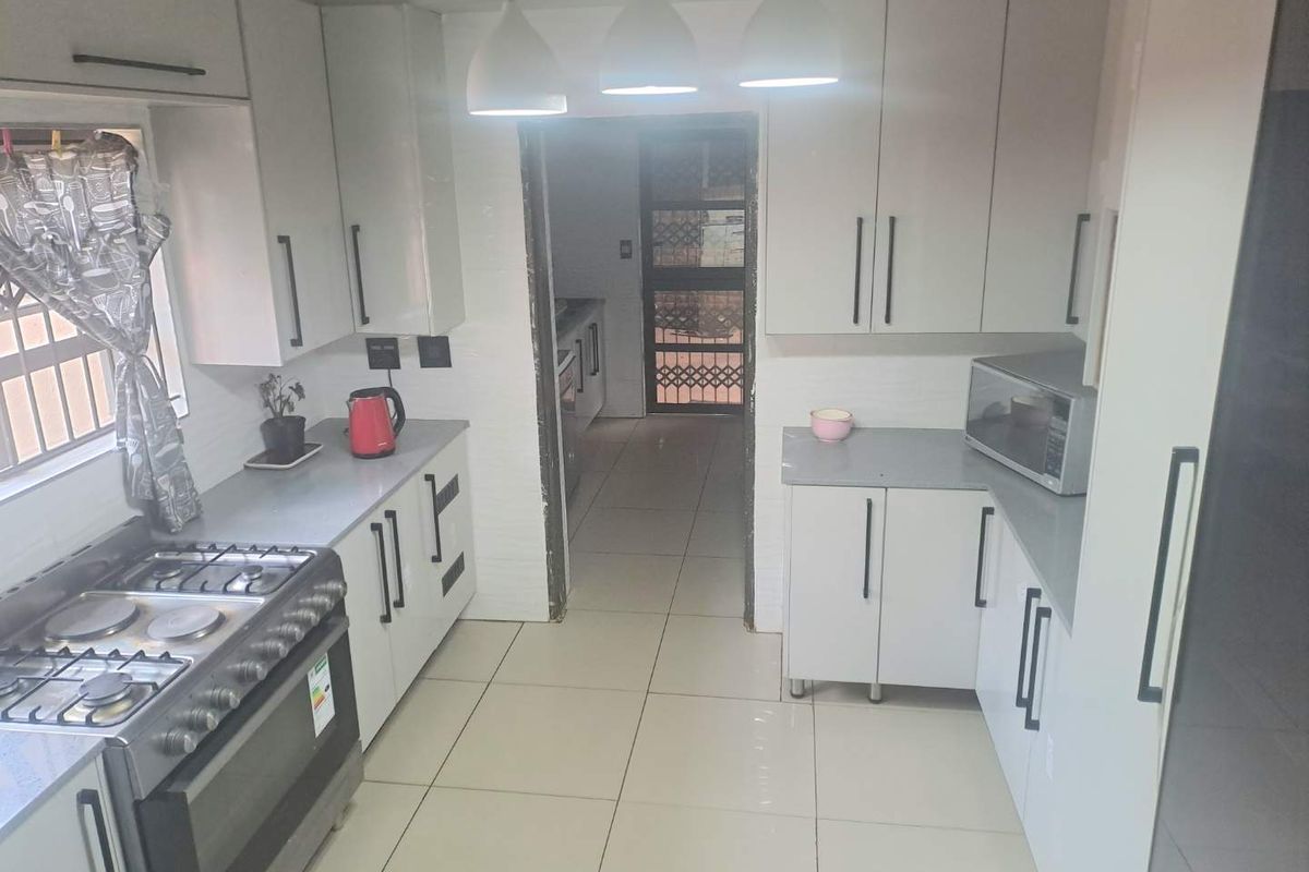 A functional kitchen featuring modern white cabinetry, grey countertops, a gas stove with oven, and tiled flooring, leading to a rear exit.