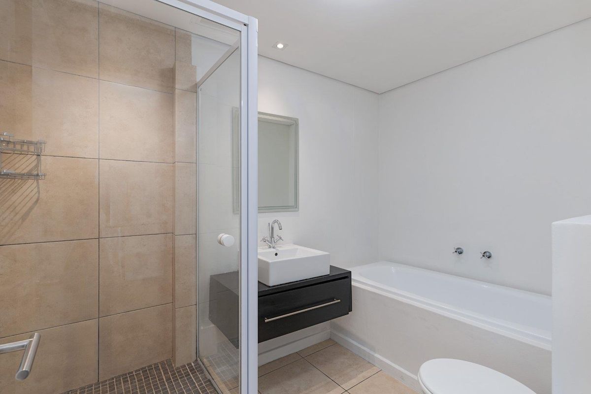 Modern bathroom featuring a glass-enclosed shower, wall-mounted vanity with vessel sink, and a built-in bathtub with neutral tiling.