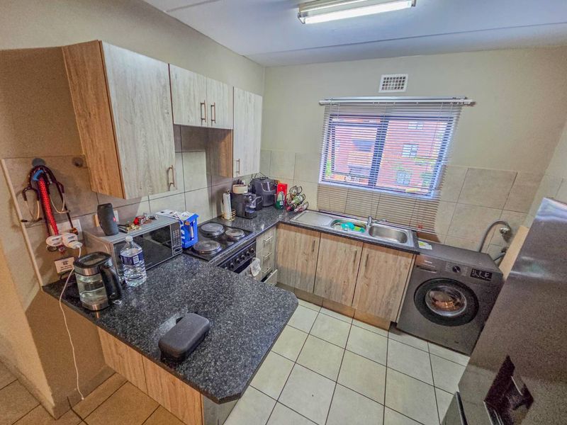 Compact kitchen featuring laminate cabinetry, granite countertops, electric hob, built-in oven, and double bowl sink with tiled flooring.