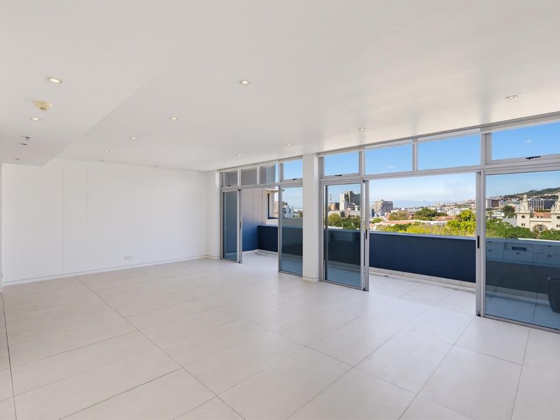 Spacious, light-filled living area featuring large format floor tiles, recessed lighting, and expansive sliding glass doors opening onto a private balcony with city views.