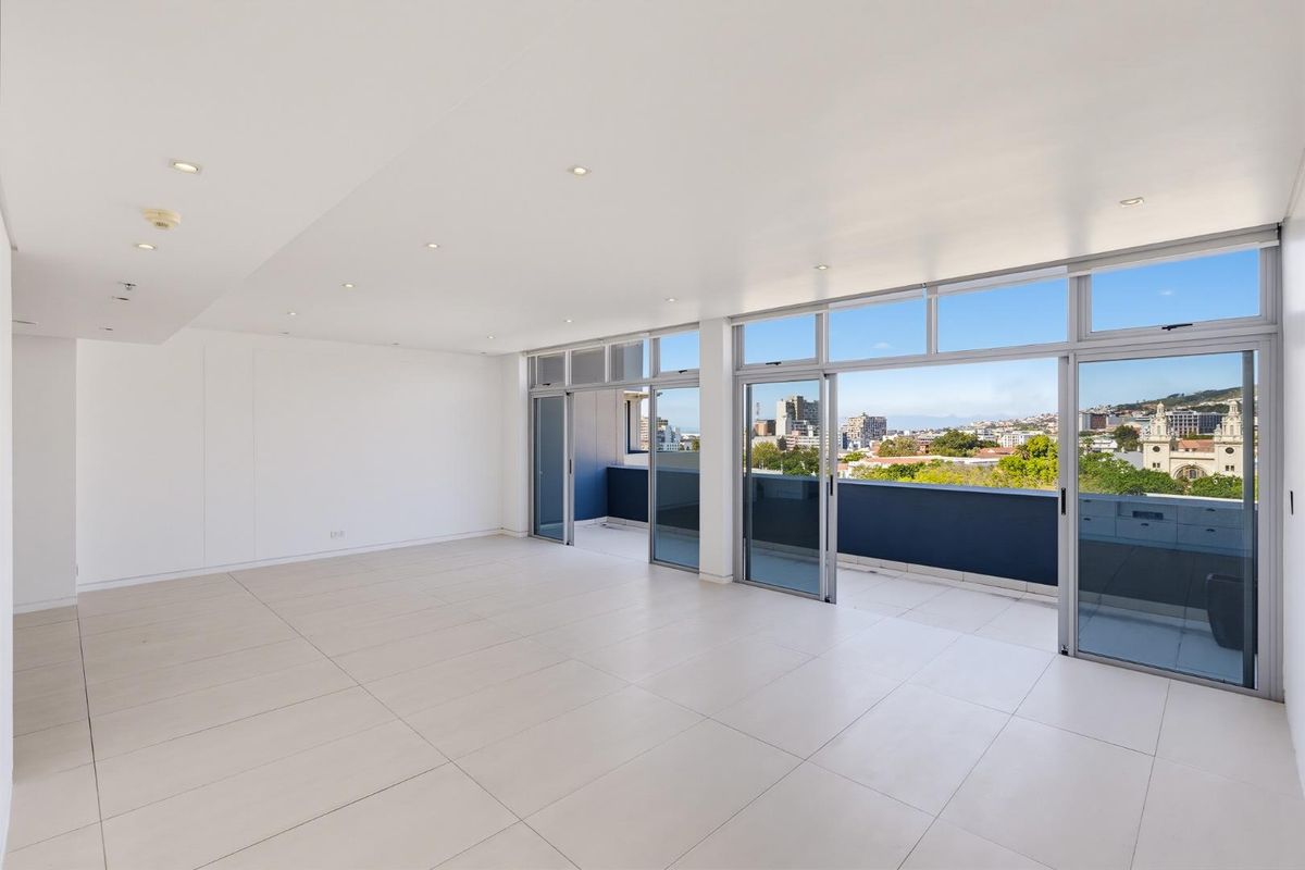 Spacious, light-filled living area featuring large format floor tiles, recessed lighting, and expansive sliding glass doors opening onto a private balcony with city views.