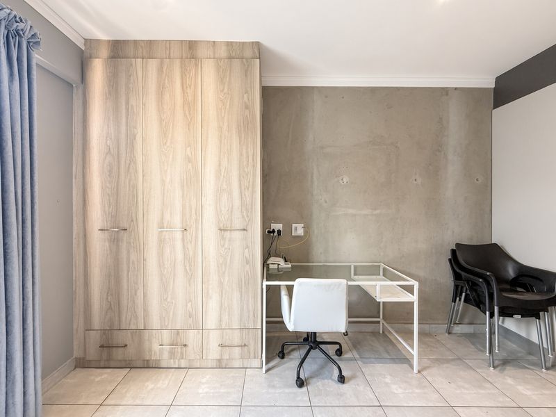 A modern bedroom featuring a large built-in wood-finish wardrobe, tiled flooring, and a contemporary exposed concrete feature wall.