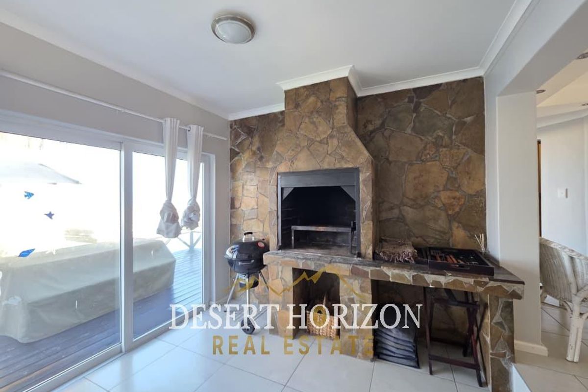 Indoor entertainment area featuring a built-in stone fireplace and braai, tiled flooring, and large sliding glass doors leading to an outdoor deck.