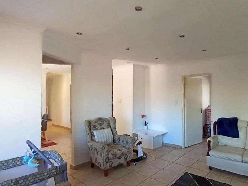 A living room area featuring tiled flooring and recessed downlights, with an open-plan layout leading to adjacent rooms.
