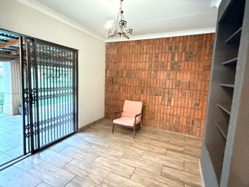 Living area featuring an exposed brick accent wall, built-in shelving, tiled flooring, and sliding glass doors leading to an outdoor space.