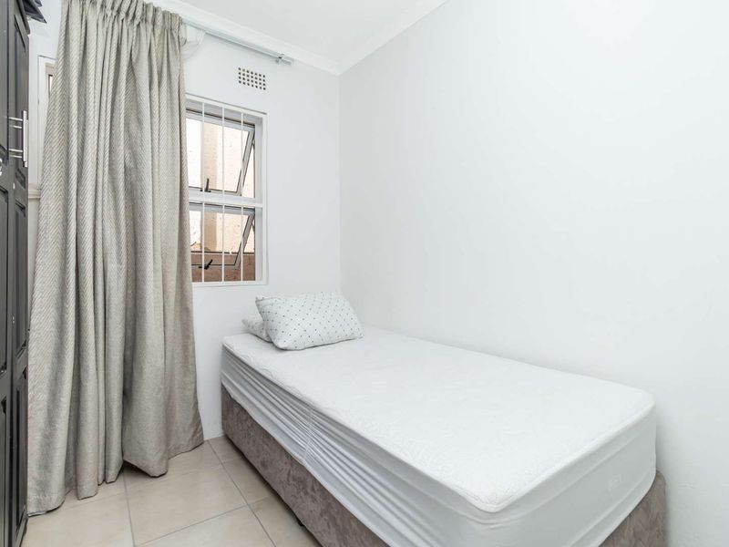 A compact bedroom featuring tiled flooring, a top-hung window with security bars, and a built-in wardrobe.