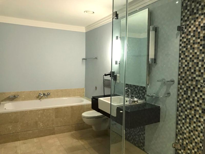 A modern bathroom featuring a built-in bathtub, wall-mounted toilet, floating vanity, and a glass-enclosed shower with decorative mosaic tile accents.