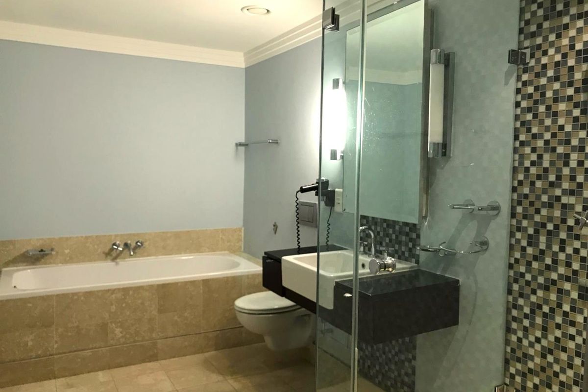 A modern bathroom featuring a built-in bathtub, wall-mounted toilet, floating vanity, and a glass-enclosed shower with decorative mosaic tile accents.