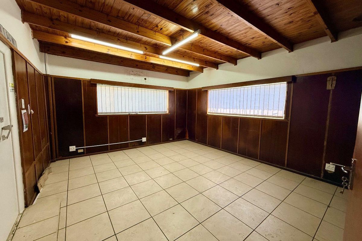 An empty interior room featuring exposed timber beam ceilings, dark wood wall paneling, and tiled flooring with integrated fluorescent lighting.