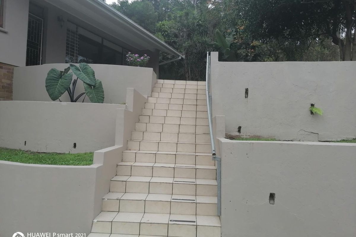 Exterior rear view featuring a tiled staircase with a metal handrail, leading up to the main house structure with tiered retaining walls.