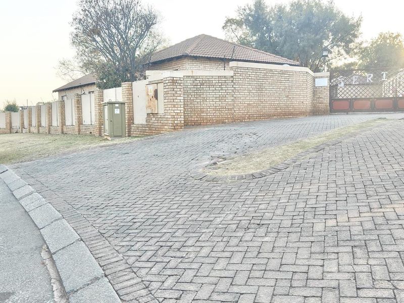 Street view of the property entrance featuring a paved driveway, brick boundary wall, and secure metal gate access.
