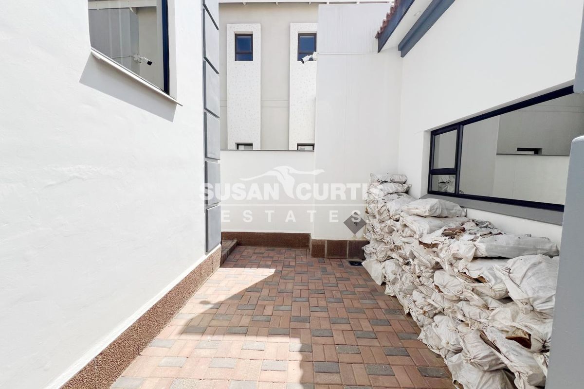 A paved side courtyard or utility area featuring modern white exterior walls, dark-framed windows, and a clean, functional layout.