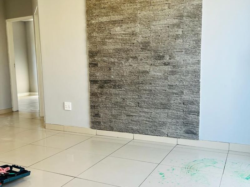 An empty living area featuring a prominent stacked stone feature wall and light-colored porcelain floor tiles.